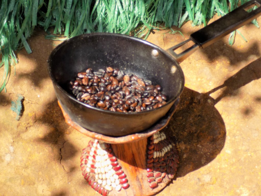 This photo shows coffee beans roasting in a skillet over a charcoal burner on the ground