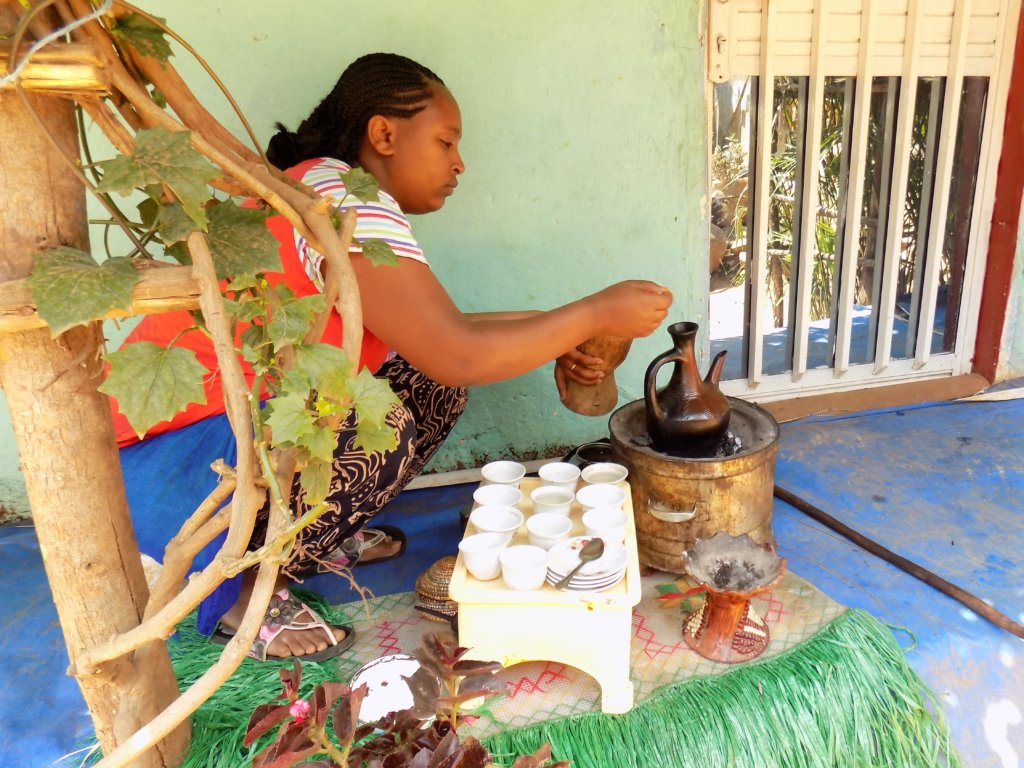 This photo shows a lady brewing coffee in a special pot over a charcoal fire