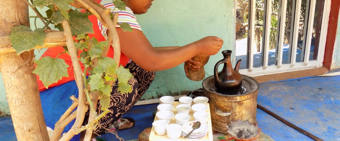 This photo shows a lady brewing coffee in a special pot over a charcoal fire