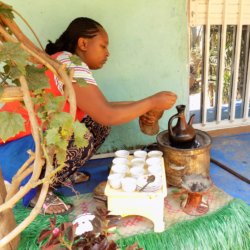 This photo shows a lady brewing coffee in a special pot over a charcoal fire