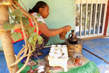 This photo shows a lady brewing coffee in a special pot over a charcoal fire