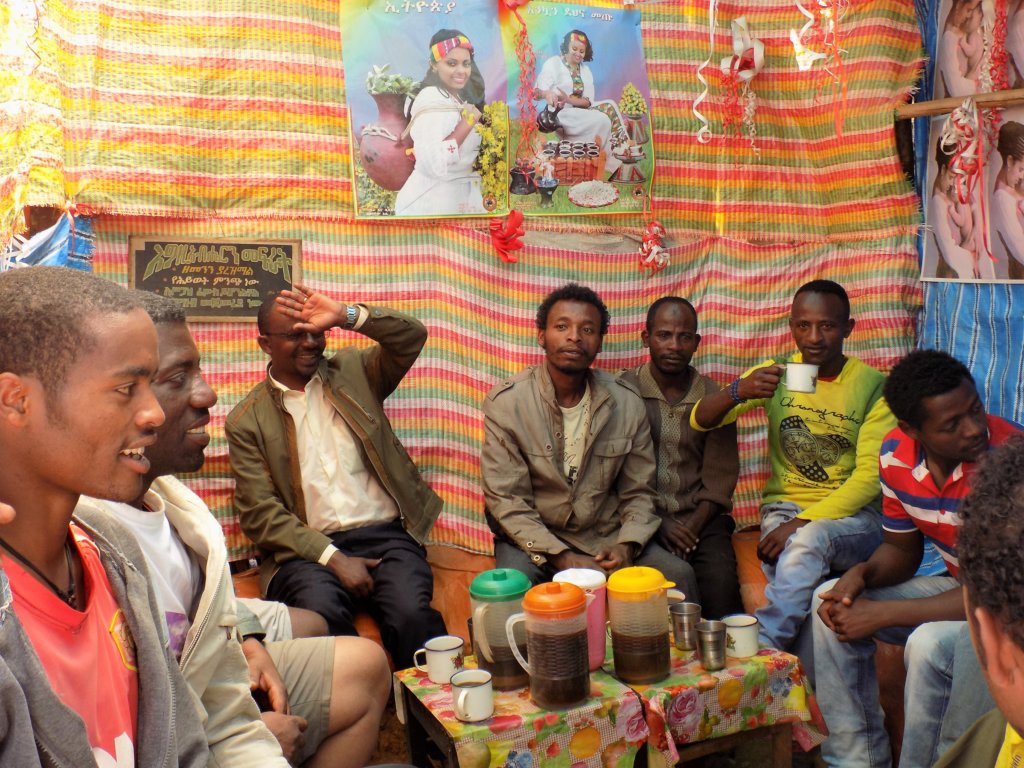 This photo shows a group of Ethiopian men sitting in a tent-like structure drinking the local brew, talla.