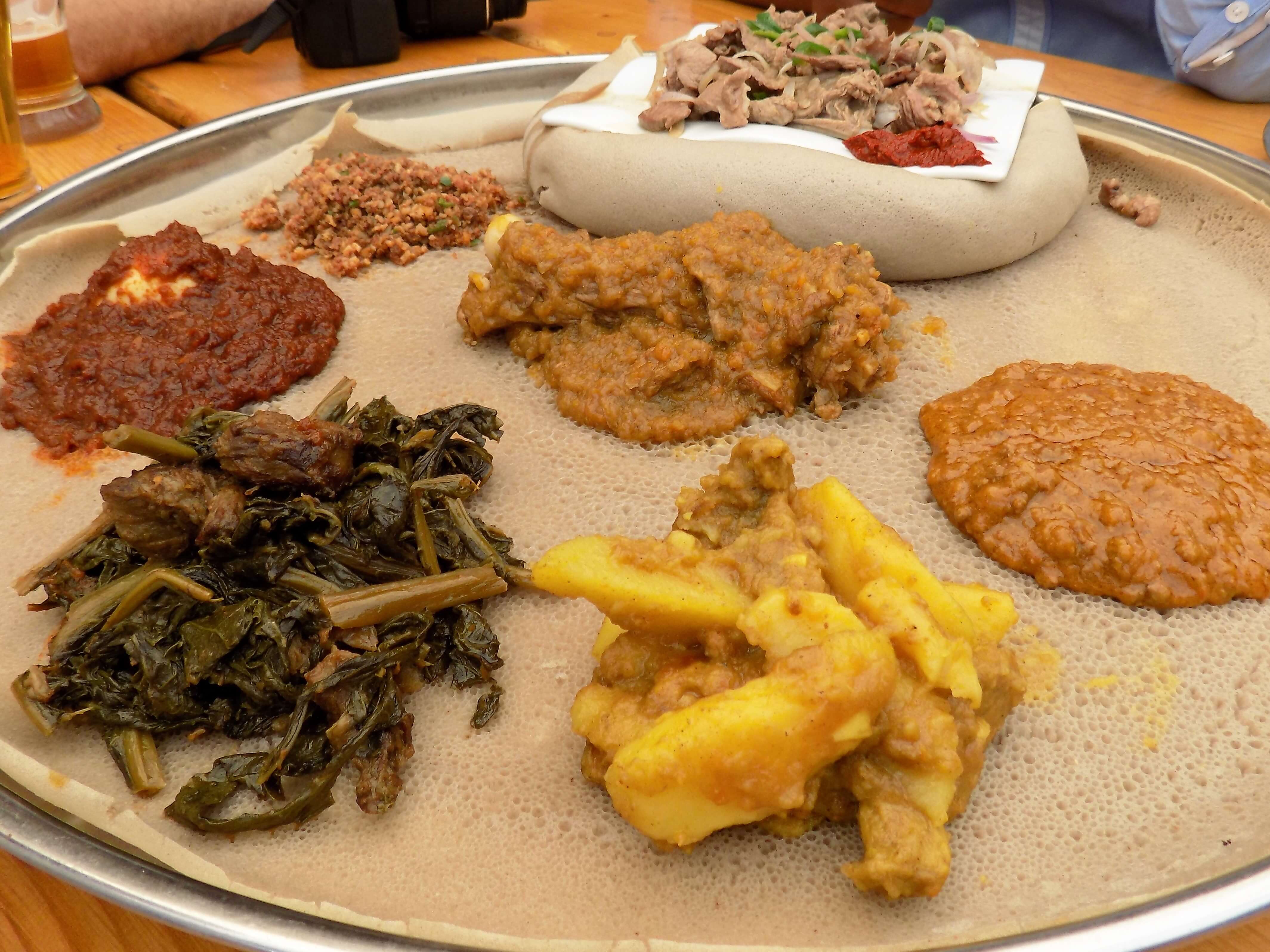 This photo shows a selection of spicy stews and bean pastes served on an 'injera plate' accompanied by rolls of injera