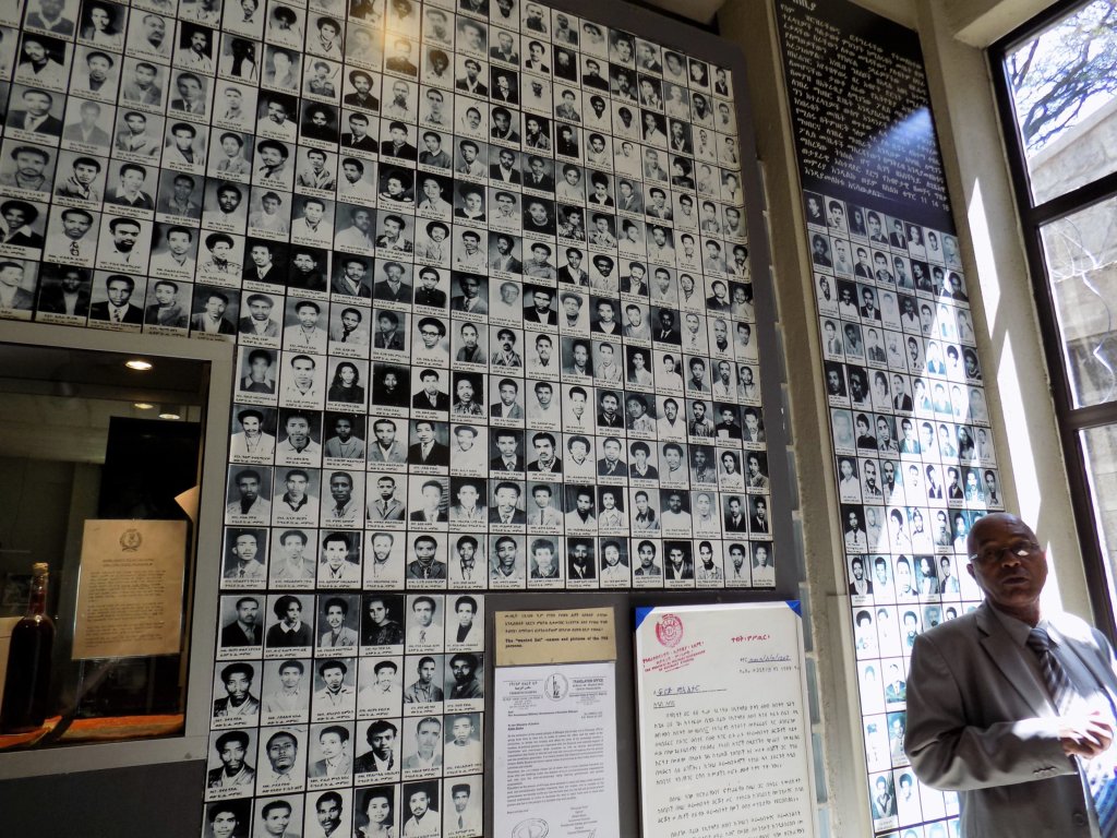 This photo shows Our guide in front of a wall of photos of victims of the Derg