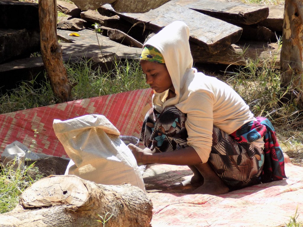 This photo shows a young girl crouching on the ground sieving stone to be made into cement