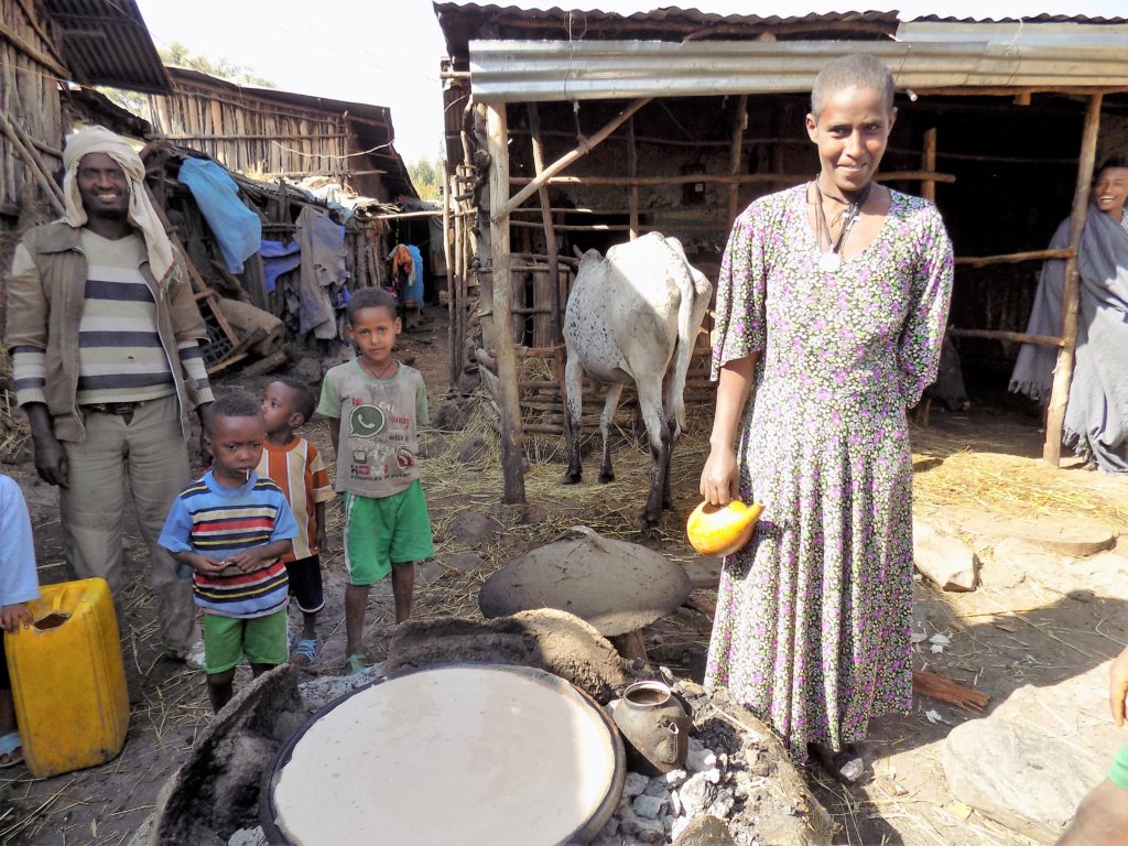 This photo shows a lady cooking injera on an outdoor fire watched by her children