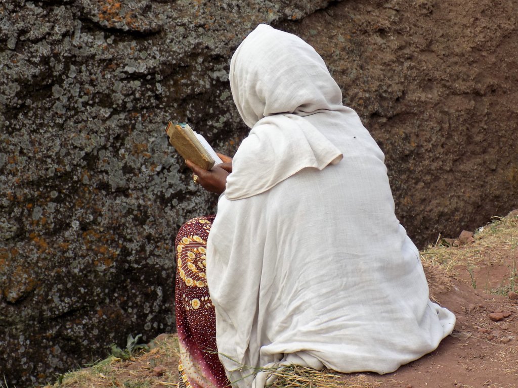 This photo shows a lady sitting outside one of the rock-hewn churches of Lalibela reading her bible
