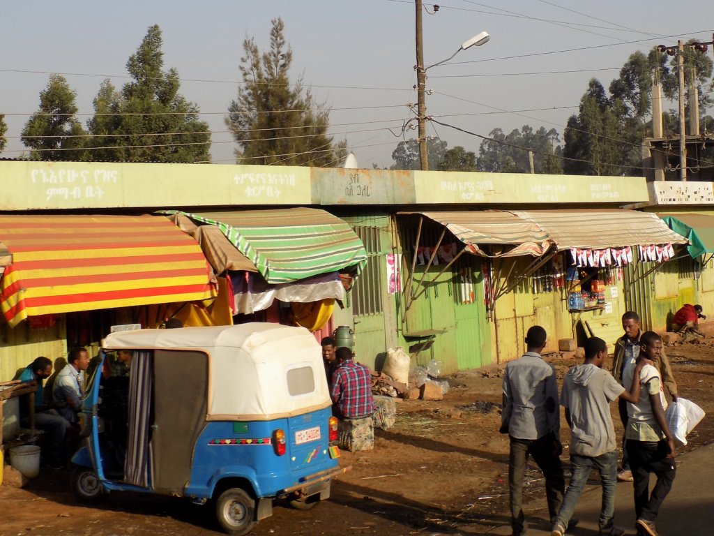 This picture shows a blue and white tuk tuk and people going about their business in Debre Markos
