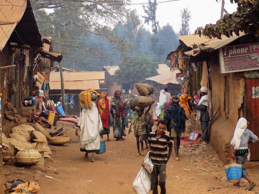 This photo shows a busy village street with baskets for sale and lots of people doing their shopping