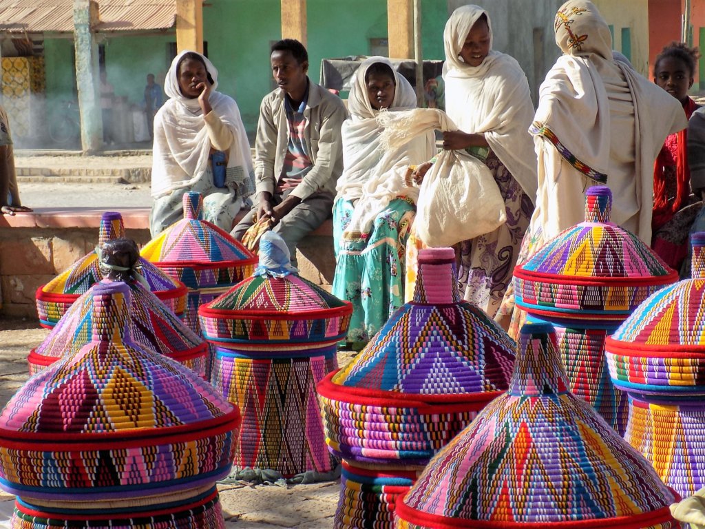 This photo shows a group of Ethiopian ladies (and one man) dressed in traditional white robes sitting on a low wall behind their baskets