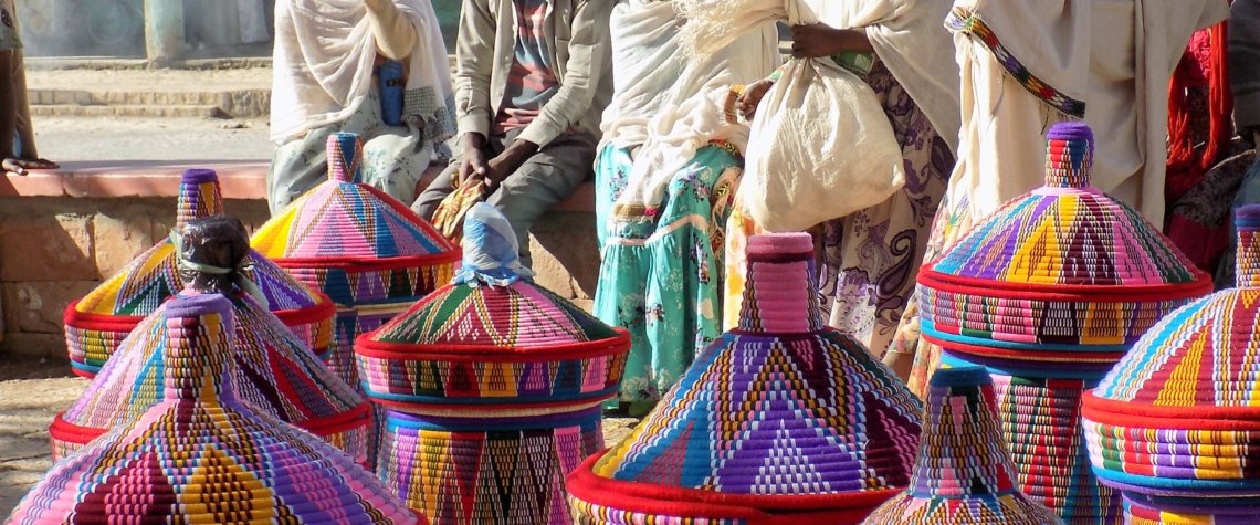 This photo shows a group of Ethiopian ladies (and one man) dressed in traditional white robes sitting on a low wall behind their baskets