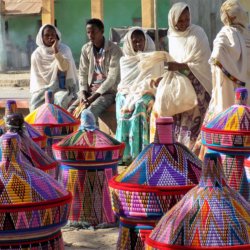 This photo shows a group of Ethiopian ladies (and one man) dressed in traditional white robes sitting on a low wall behind their baskets