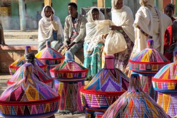 This photo shows a group of Ethiopian ladies (and one man) dressed in traditional white robes sitting on a low wall behind their baskets