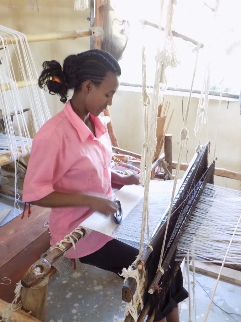 This photo shows a lady using a wooden hand loom to weave cream woollen fabric