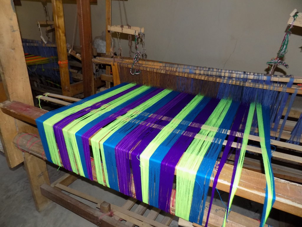 This photo shows green blue and purple threads on a wooden loom