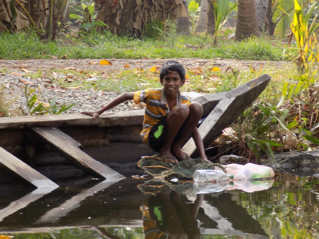 This photo shows a young boy crouched on the side of his boat checking to see if he's caught any fish