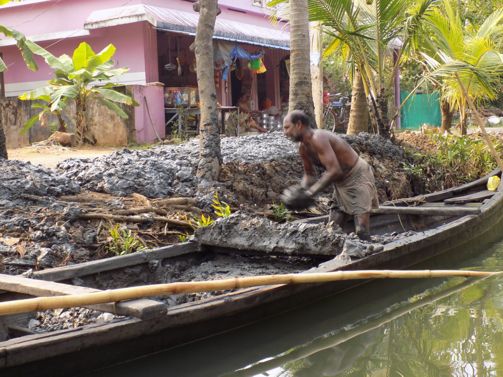 This photo shows a man in a boat full of mud throwing it on to the bank to fertilise the trees