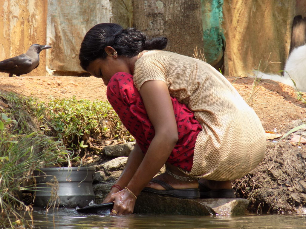 This photo shows a lady kneeling on the banks of a backwater washing her cooking pots
