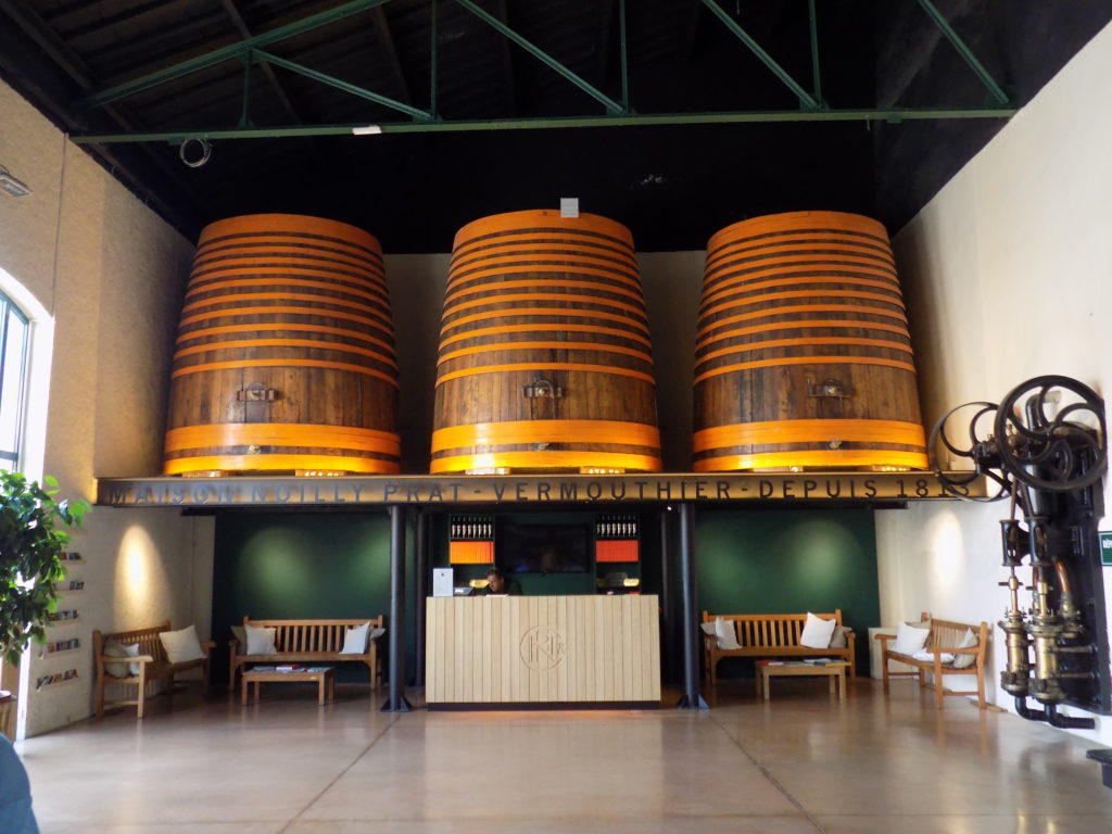 This picture shows the entrance hall of the Noilly Prat distillery with the reception desk and three huge barrels above it.