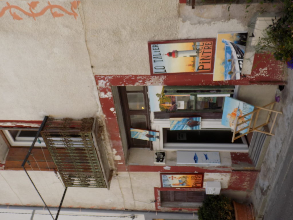 This photo shows an artist's studio in the back streets of Marseillan. There are colourful canvases displayed outside