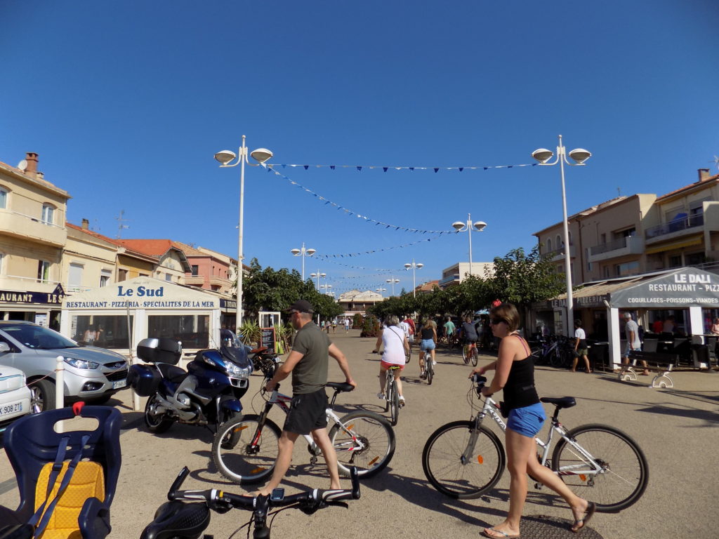 This photo shows the main square in Valras Plage with several people cycling through