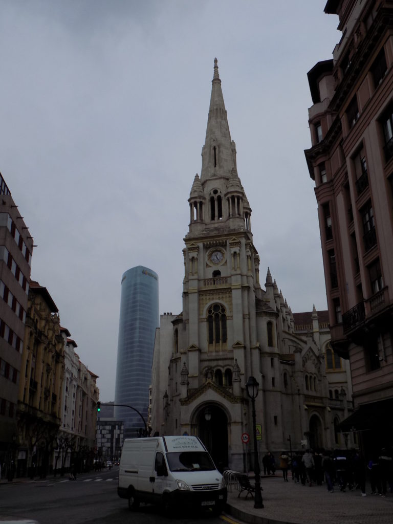This photo shows an old Gothic church in the foreground with a tall modern office building in the background.