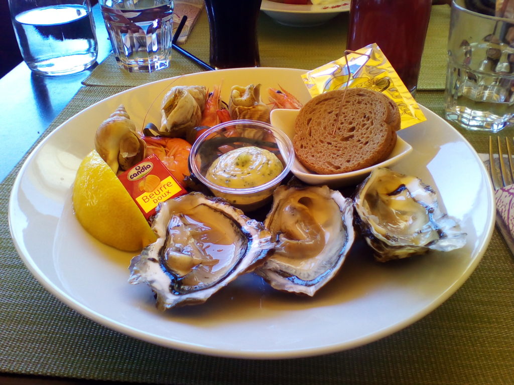 This photo shows a plate of fresh oysters, prawns and molluscs served with aioli and brown bread