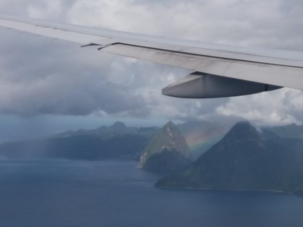 This image shows a rainbow appearing between two mountains. It was taken from the window on our flight from London Gatwick to Port of Spain, Trinidad. The mountains are on the island of St. Lucia. We briefly stopped there to drop some passengers off.