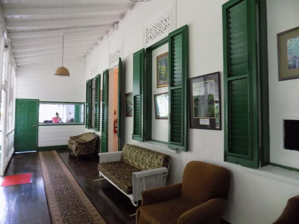 An image of the colonial-style reception area of the main house at the Asa Wright Centre, Trinidad. The white walls and green paintwork show off the dark, antique furniture.
