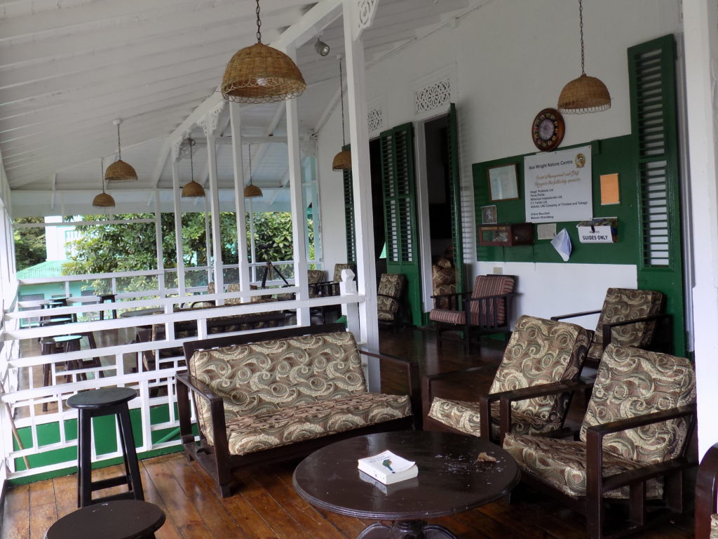 An image of the colonial-style verandha of the main house at the Asa Wright Centre, Trinidad. The white walls and green paintwork show off the dark, antique furniture.