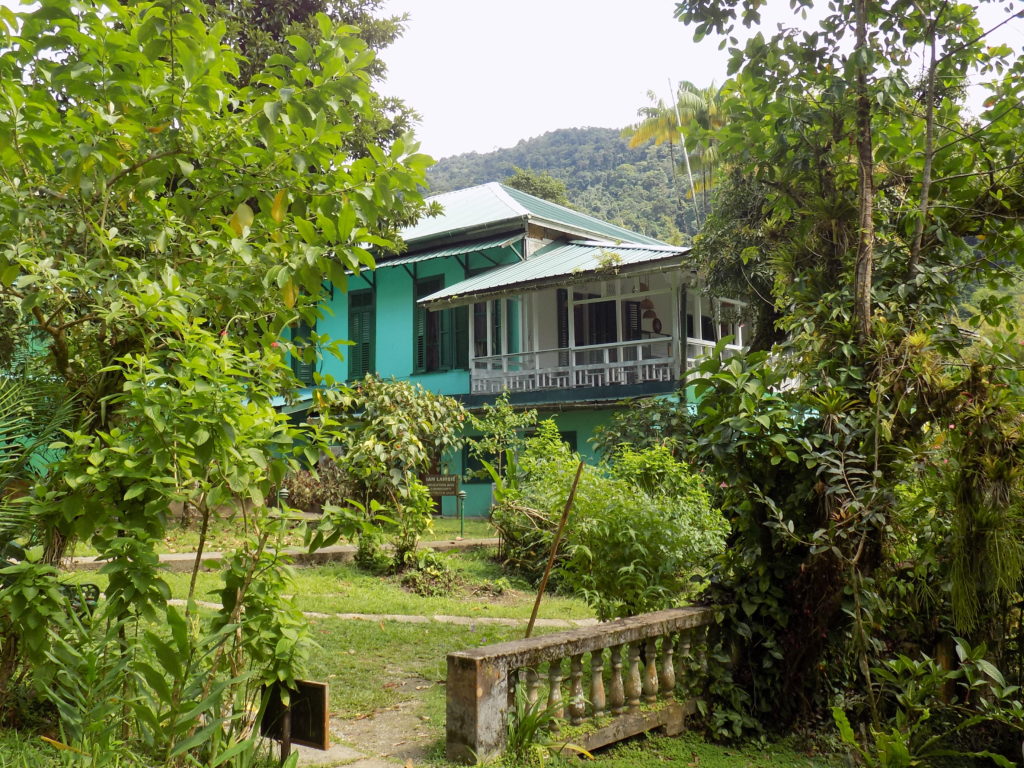 This photo shows the main house painted green and set amongst lush tgrees and shrubs