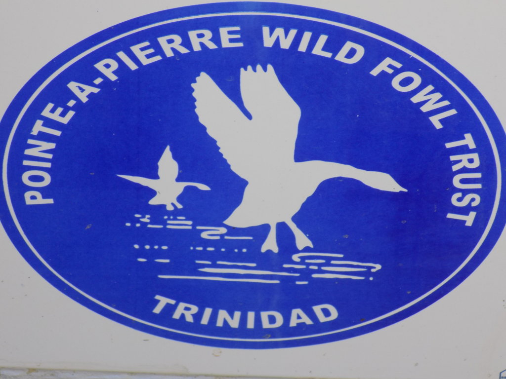 This photo shows the The Pointe-a-Pierre Wildfowl Trust's logo, a blue circle with the wording in white and an outline image of a duck landing in water.