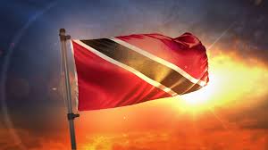 This picture shows the flag of Trinidad and Tobago, a black diagonal on a red background, flying against the backdrop of a Caribbean sunset