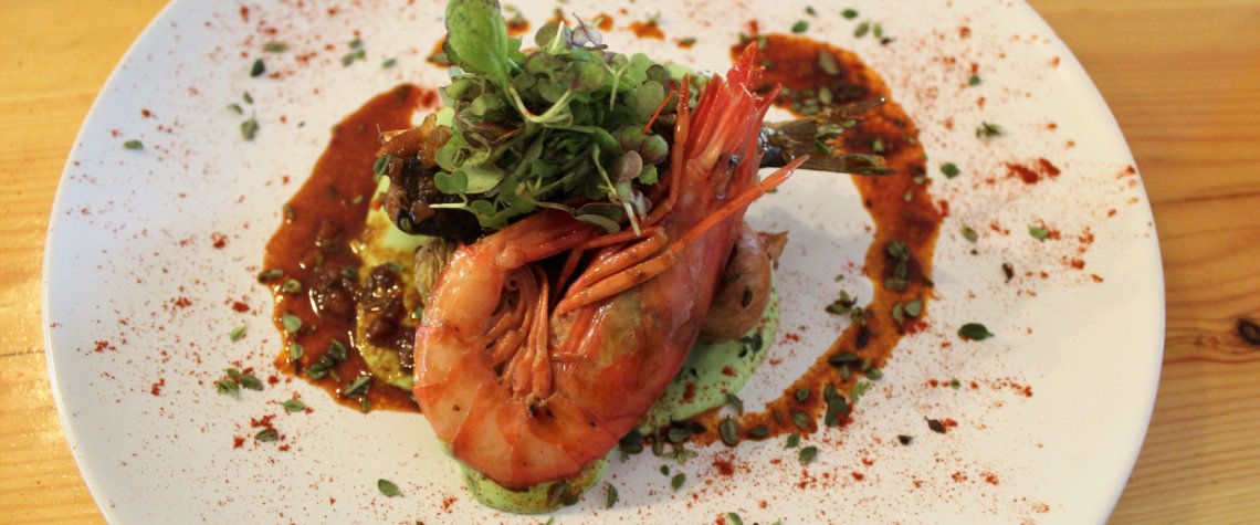 This picture shows a plate of food with a large succulent prawn on top.