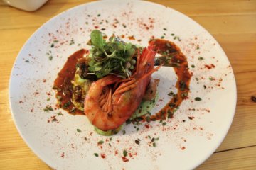 This picture shows a plate of food with a large succulent prawn on top.