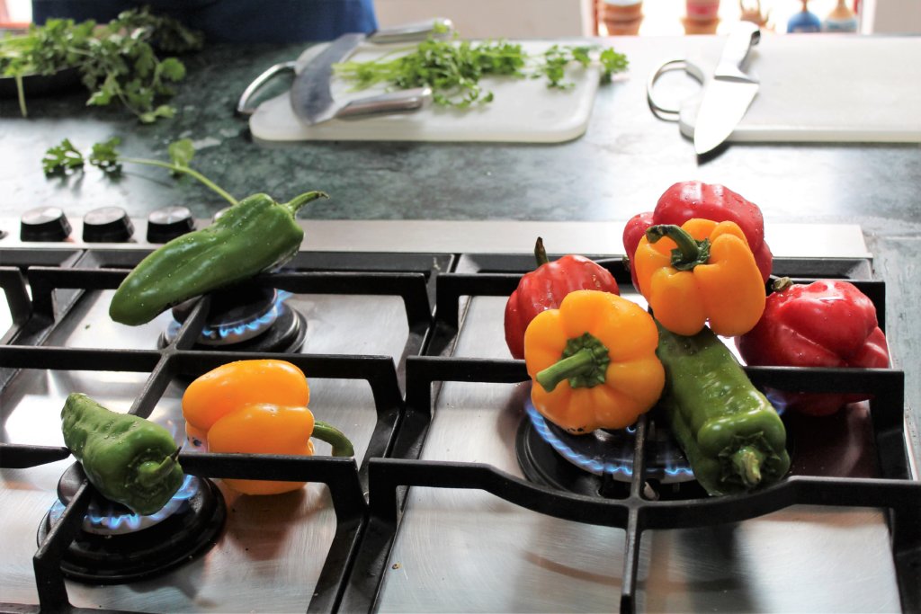 This photo shows several green, yellow and red peppers sitting directly on the gas to char them.