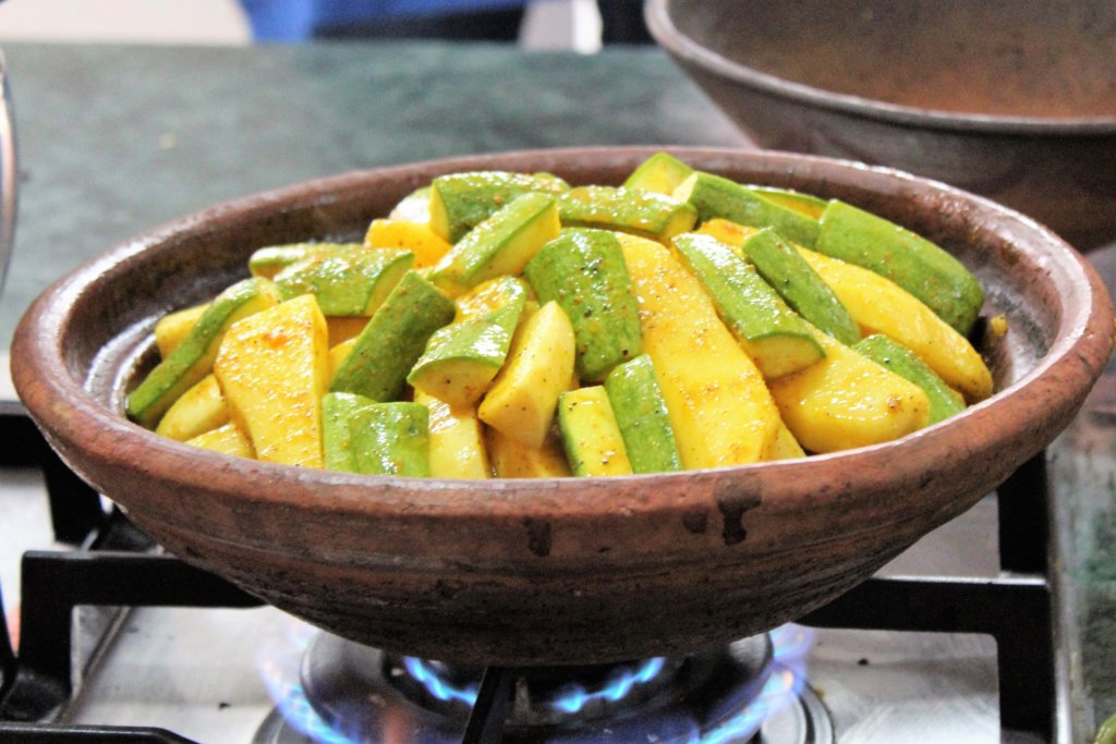 This picture shows vegetables in an uncovered tagine cooking on a gas stove