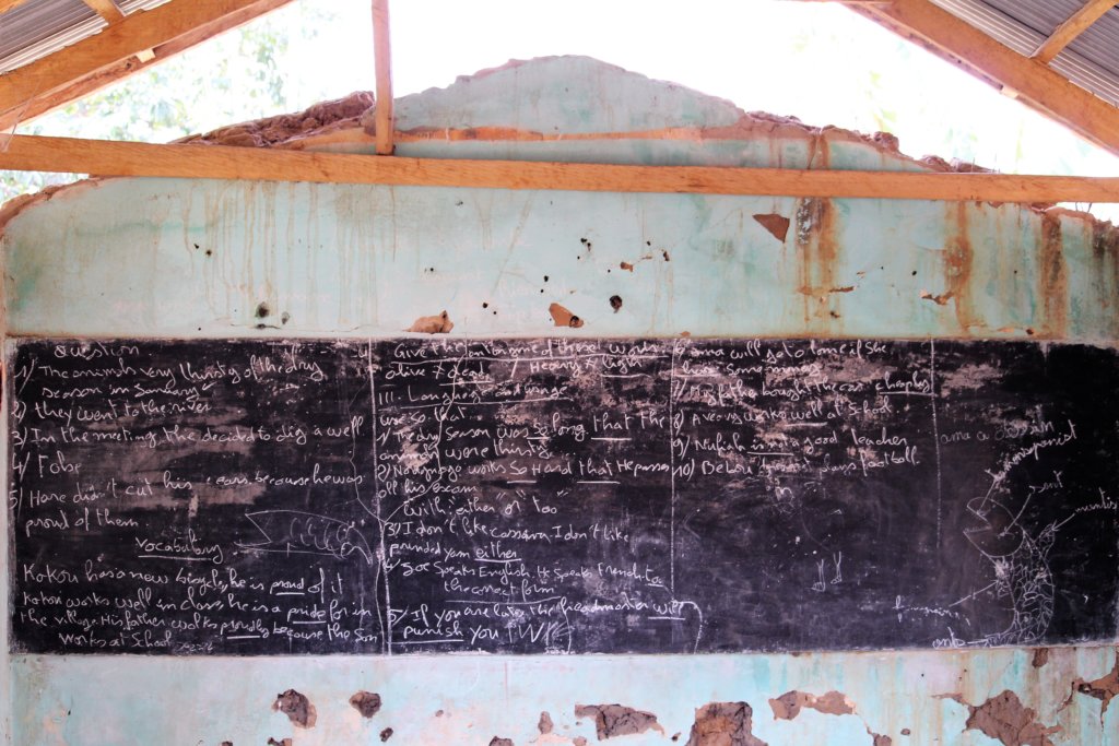 This picture shows a schoolroom with no roof, but with a lesson written on the blackboard