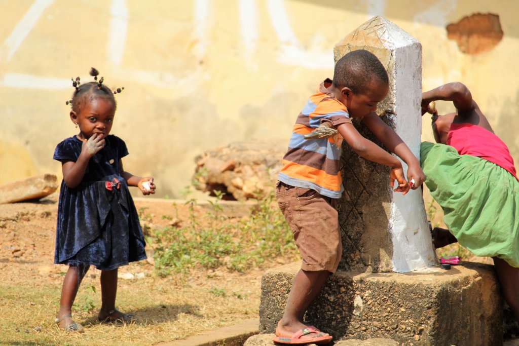 This picture shows three children at the village tap. One of them is drinking directly from the tap