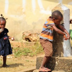 This picture shows three children at the village tap. One of them is drinking directly from the tap