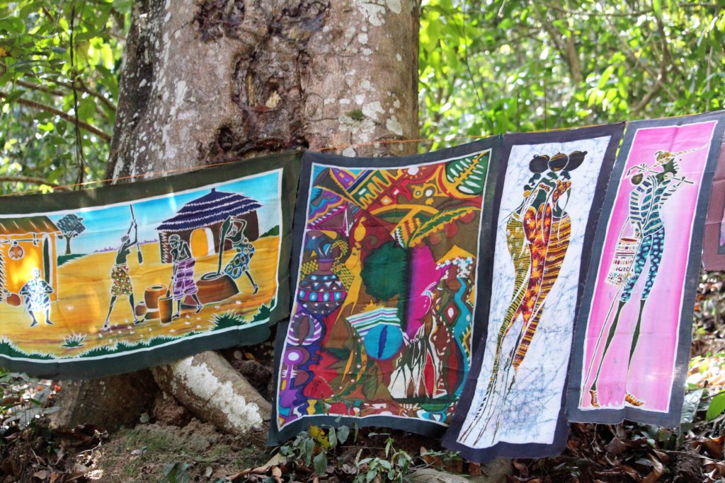 This photo shows four batik panels hanging on a line between two trees