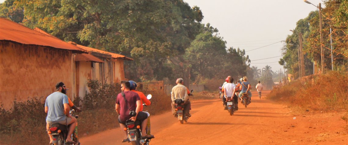 This photo shows some members of our group riding pillion along a red, dusty road