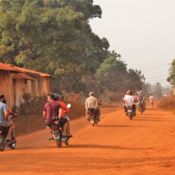 This photo shows some members of our group riding pillion along a red, dusty road