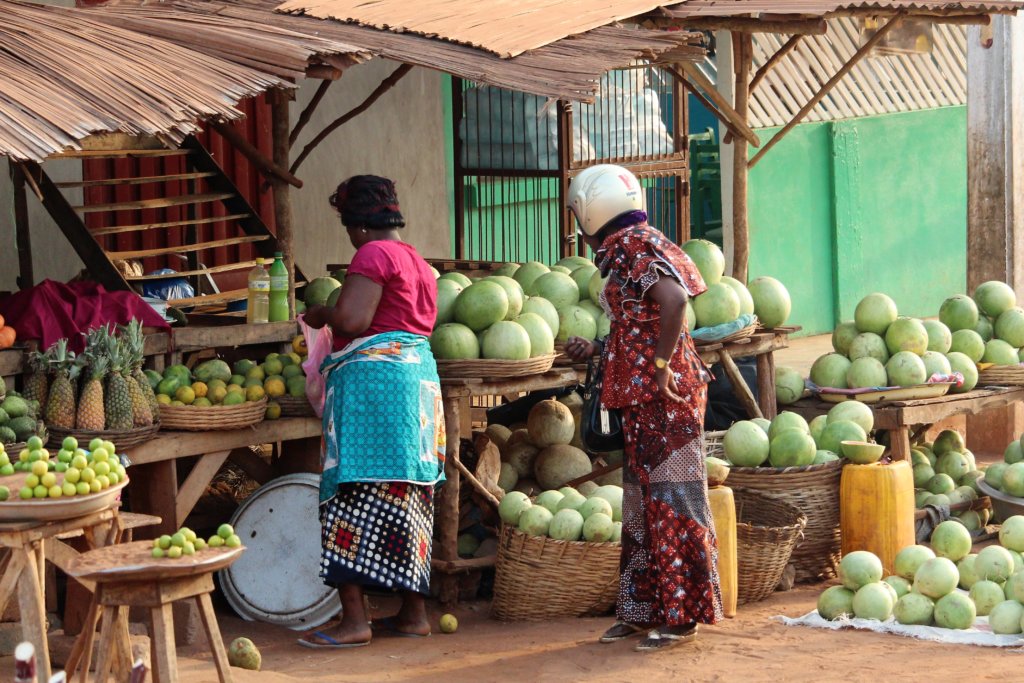 This photo shows a fruit stall with masses of watermelons on it and on the floor around it