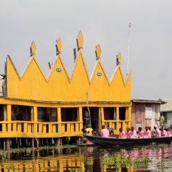 This photo shows a boat full of people dressed in pink arriving at a bright yellow-painted restaurant