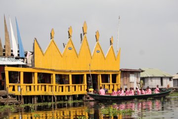 This photo shows a boat full of people dressed in pink arriving at a bright yellow-painted restaurant