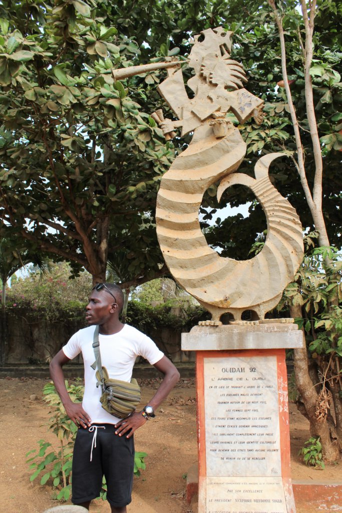 This photo shows Emmanuel standing next to a statue marking the place where the Tree of Forgetfulness was