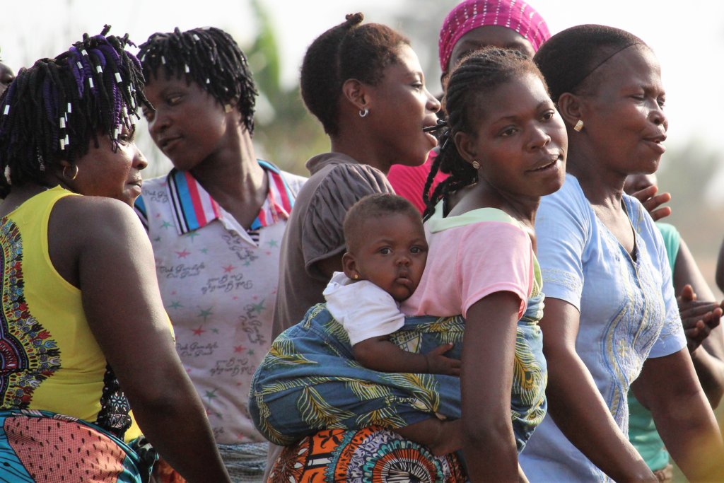 This photo shows women dancing, one of them with a baby strapped to her back