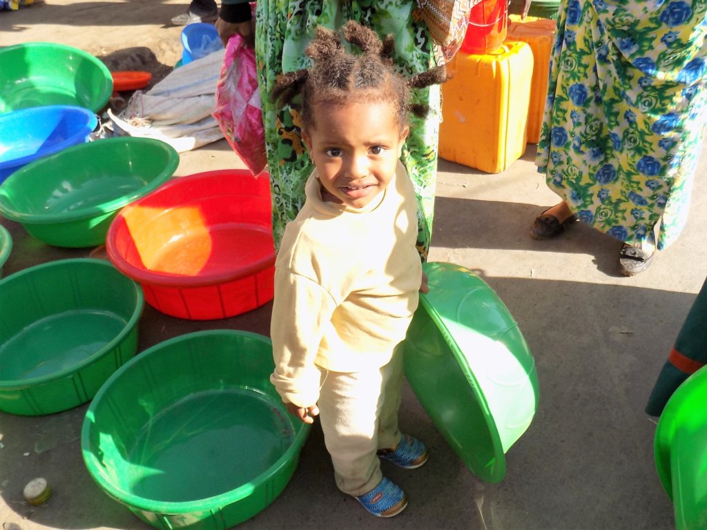 This photo shows a small girl holding a large green plastic washing-up bowl