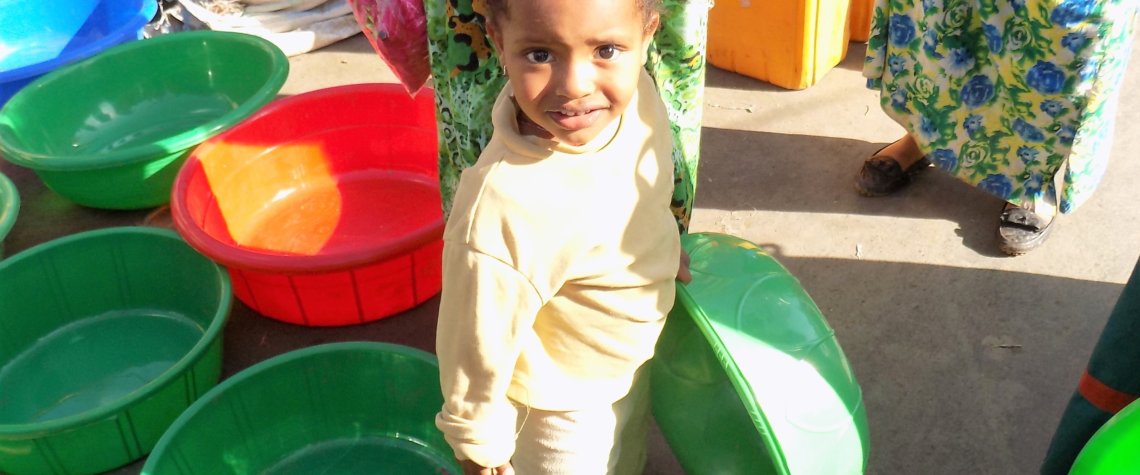 This photo shows a small girl holding a large green plastic washing-up bowl